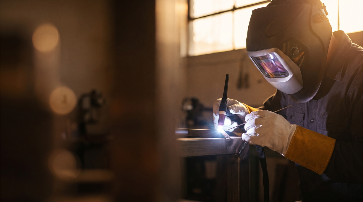 Welder TIG welding in a warm-lit workshop wearing Murbie Forge TIG welding gloves